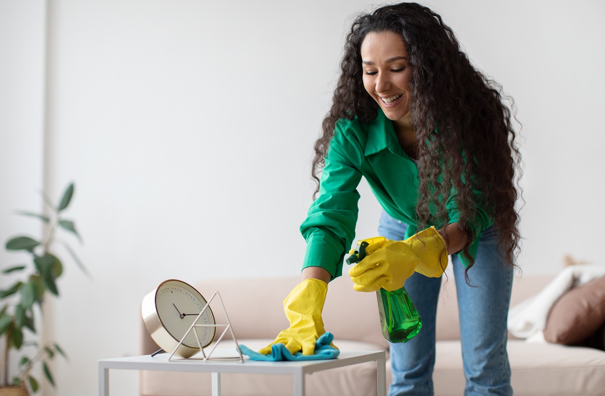 Cheerful Brunette Woman Dusting And Cleaning Desk At Home